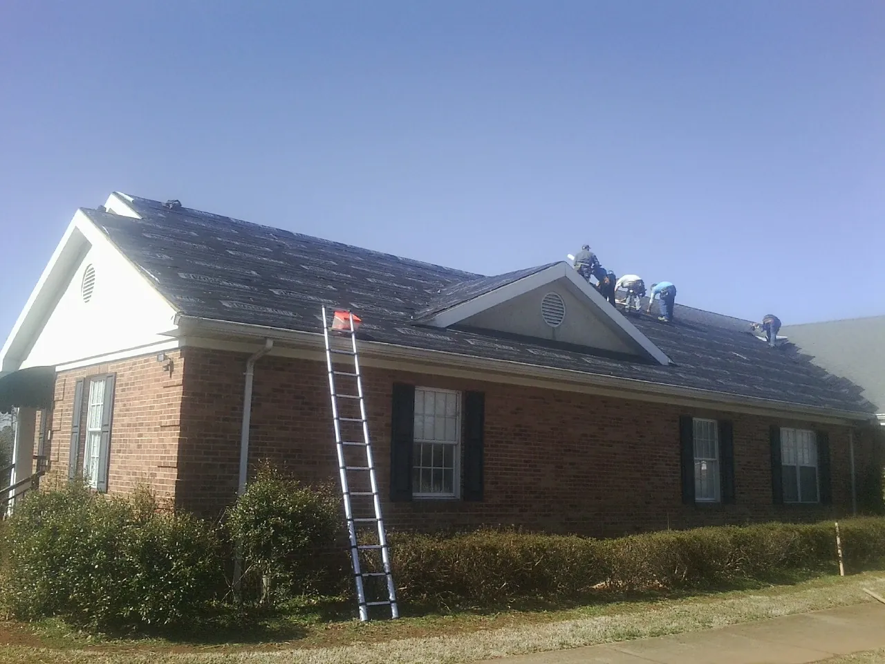 Crew tearing shingles off a brick ranch roof with a ladder set — Emergency Roof Repair work by our crew in Clarkston