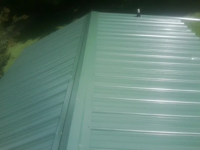 New green metal panels meeting at the ridge of a roof — Flat Roof Repair work by our crew in Clarkston