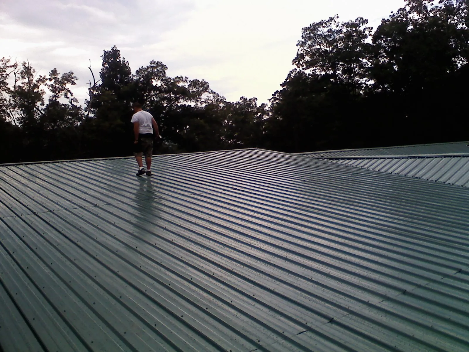 Roofer walking a wide expanse of new green metal roofing in Clarkston
